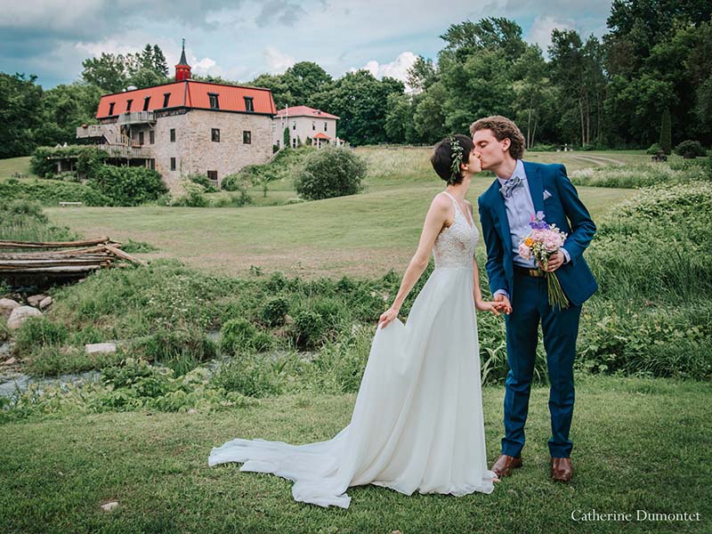Les mariés s'embrassent devant le Vieux Moulin à Rigaud